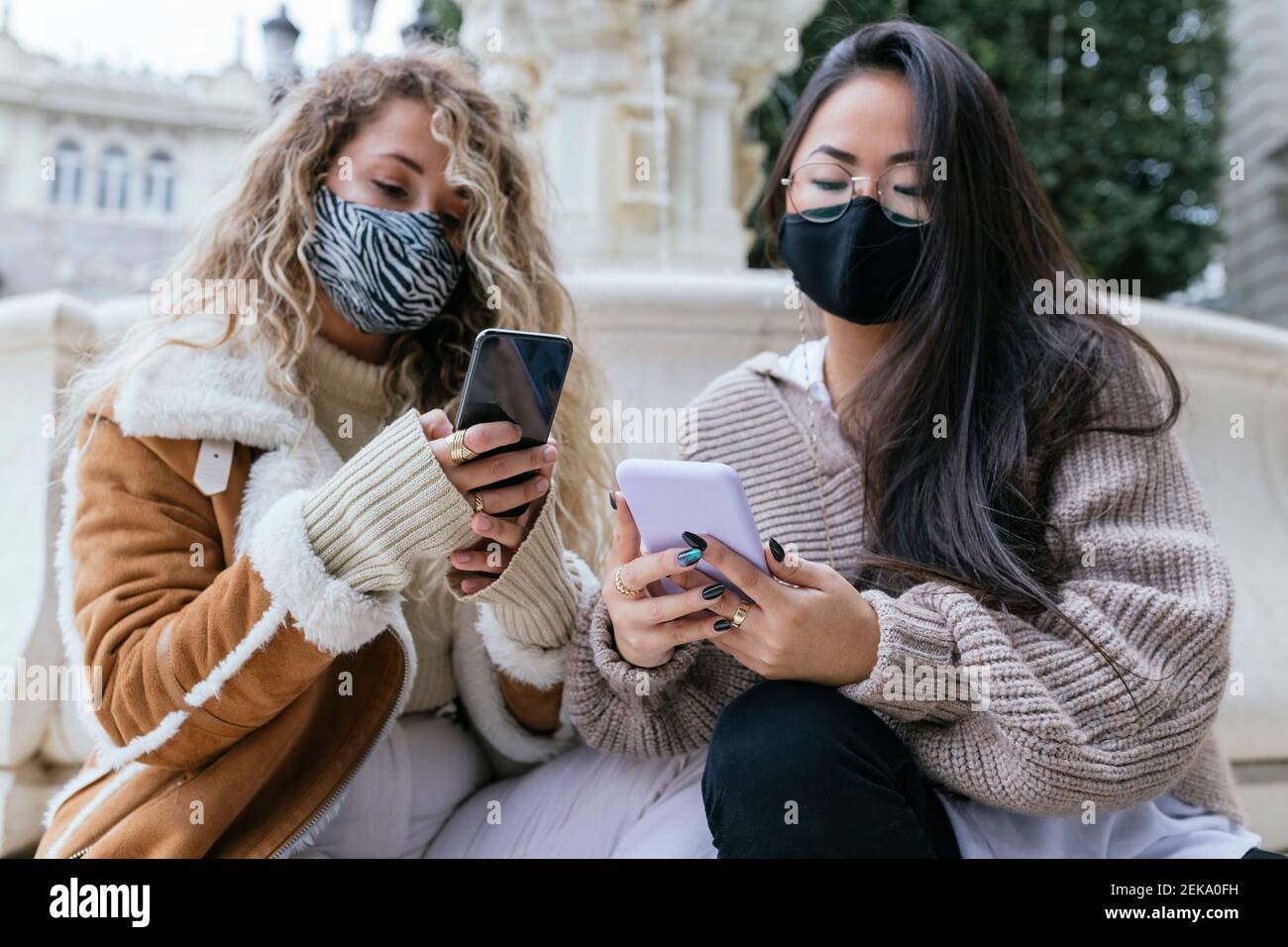 Donne multietniche che utilizzano smartphone indossando una maschera protettiva per il viso durante pandemia Foto Stock