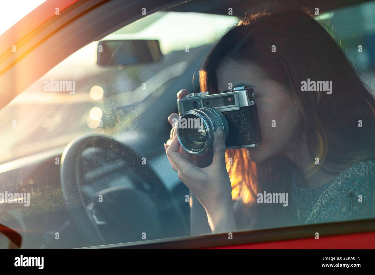 Giovane donna che fotografa dall'auto con una macchina fotografica di vecchio stile mentre è in viaggio Foto Stock