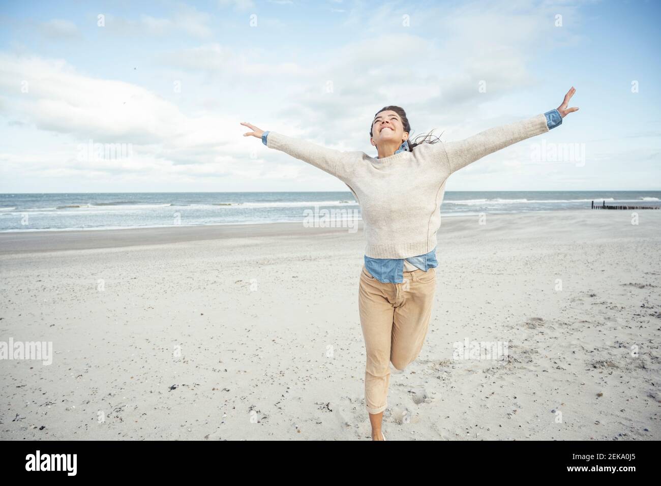 Ritratto di giovane donna che corre su spiaggia di sabbia con rialzato braccia Foto Stock