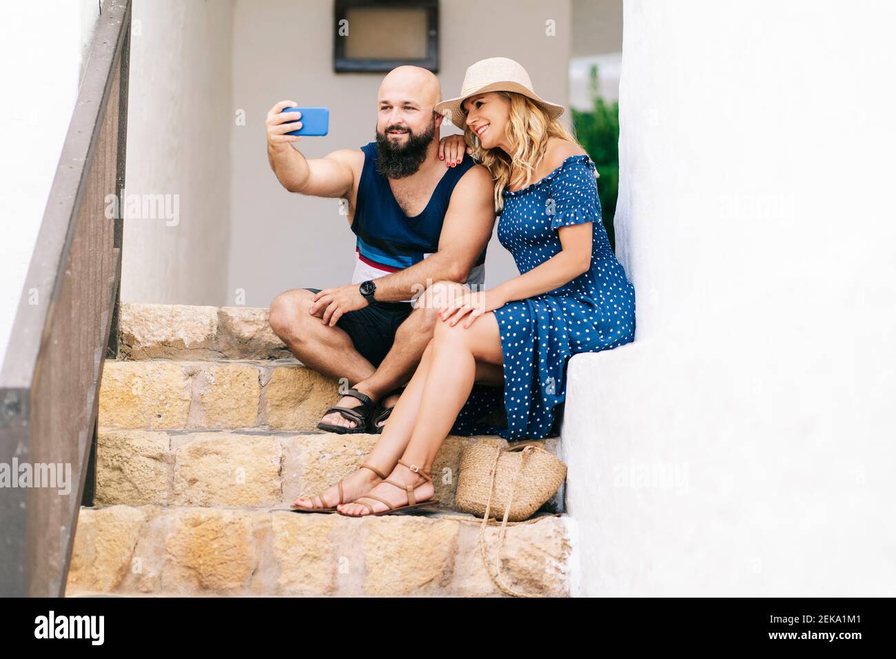 Amici che prendono selfie con smartphone mentre si siedono sui gradini al villaggio di Binibeca, Minorca, Spagna Foto Stock