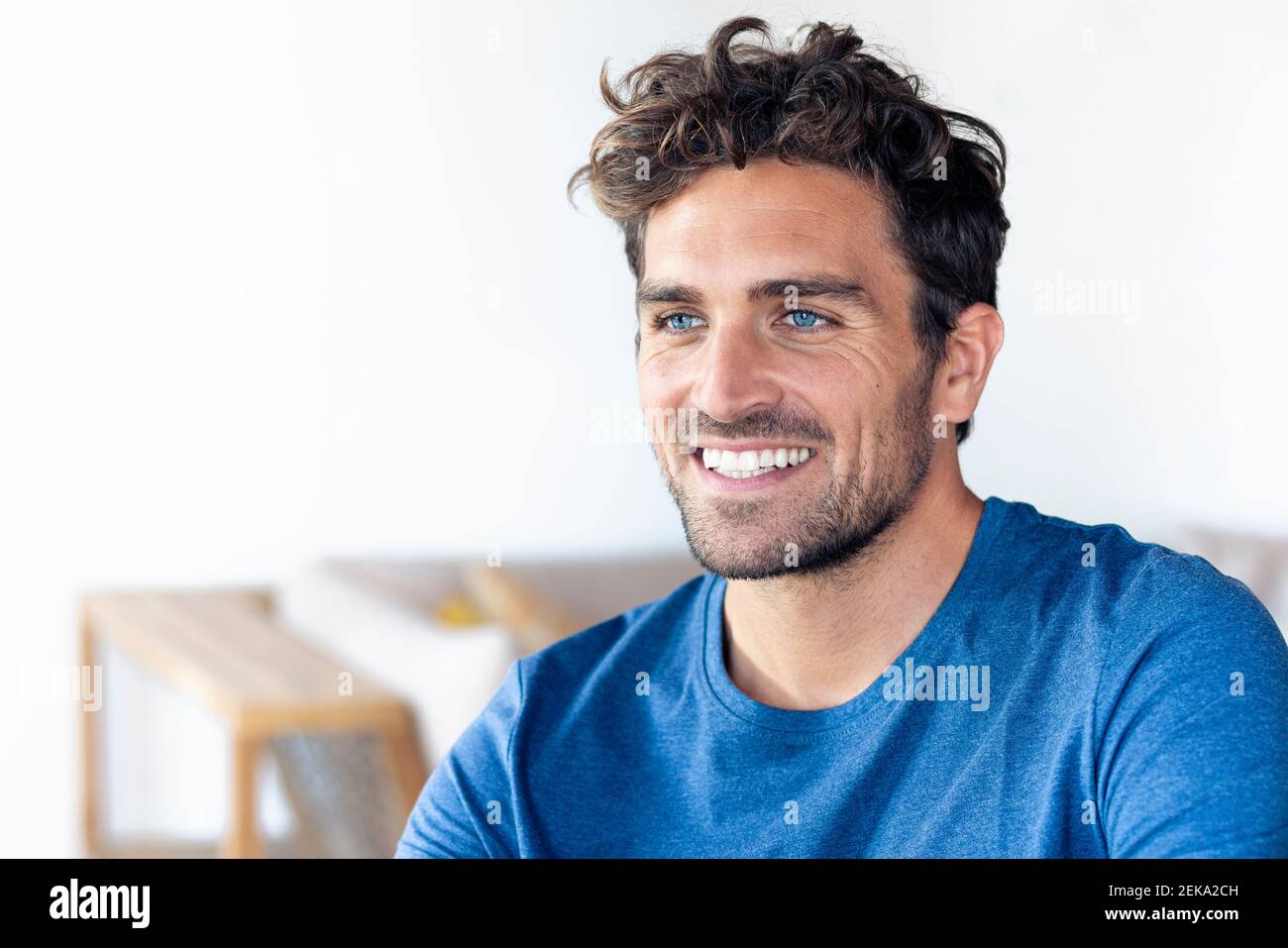 Uomo felice con gli occhi blu guardando via mentre sedendo a. casa Foto Stock