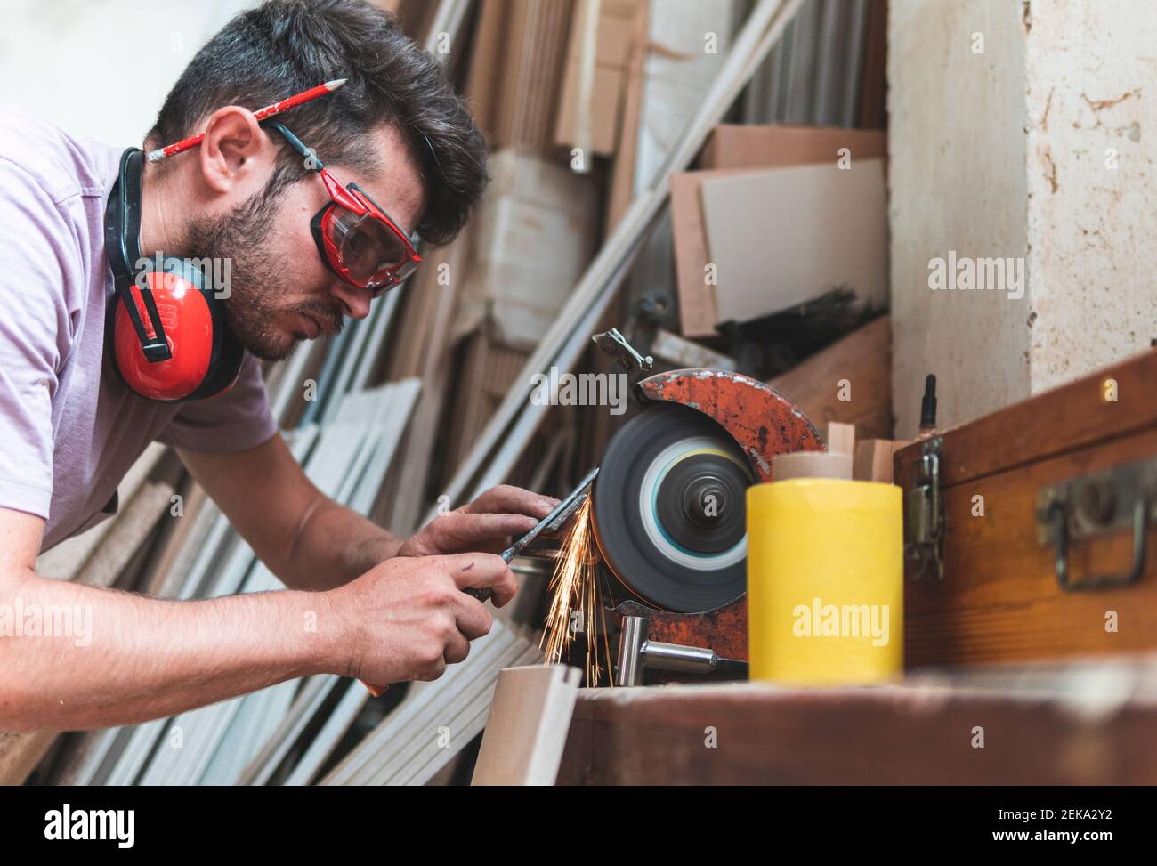 Utensile di lavoro per affilatura con falegname maschio concentrato su smerigliatrice in officina Foto Stock