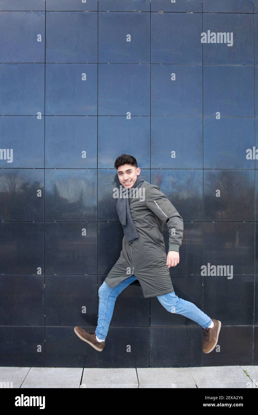 Felice uomo giovane che indossa sciarpa in piedi da parete nera Foto Stock