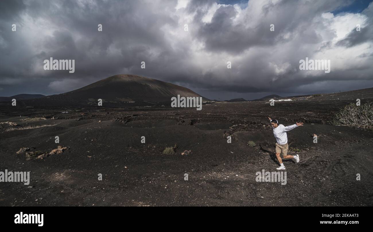 Allegro turista maschile che corre sul suolo nero al vulcano El Cuervo, Lanzarote, Spagna Foto Stock