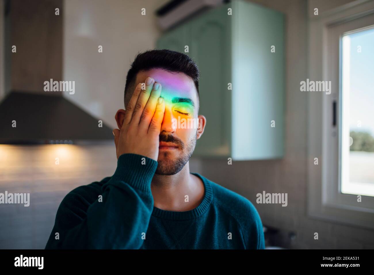 Luce arcobaleno che colpisce il volto del giovane uomo che copre un occhio con mano Foto Stock