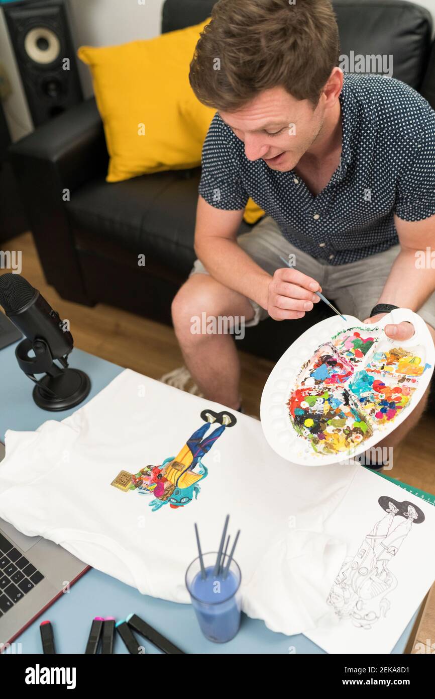 Artista che dipinge il doodle sulla t-shirt durante lo streaming dal vivo a casa Foto Stock