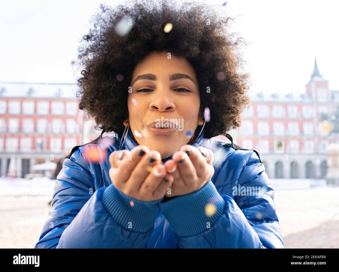 Donna afro che soffia i confetti mentre si trova in città Foto Stock