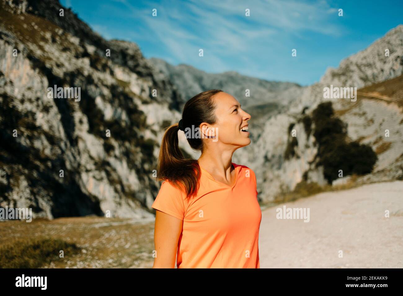 Donna sorridente che guarda la vista delle montagne mentre si trova al Cares Trail nel Parco Nazionale Picos De Europe, Asturias, Spagna Foto Stock