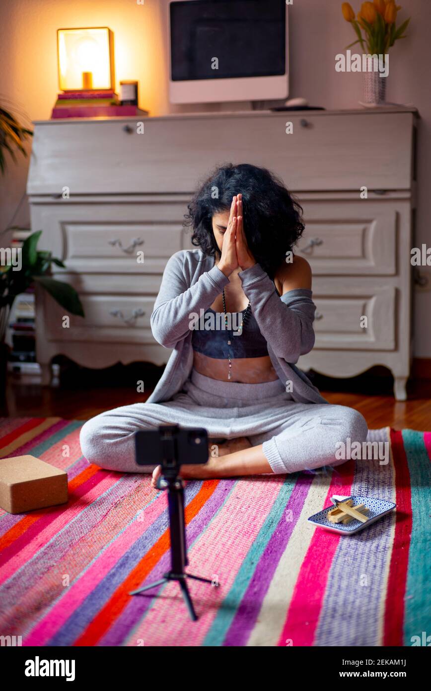 Donna spirituale con le mani aggrappate seduto a casa durante il video chiama Foto Stock