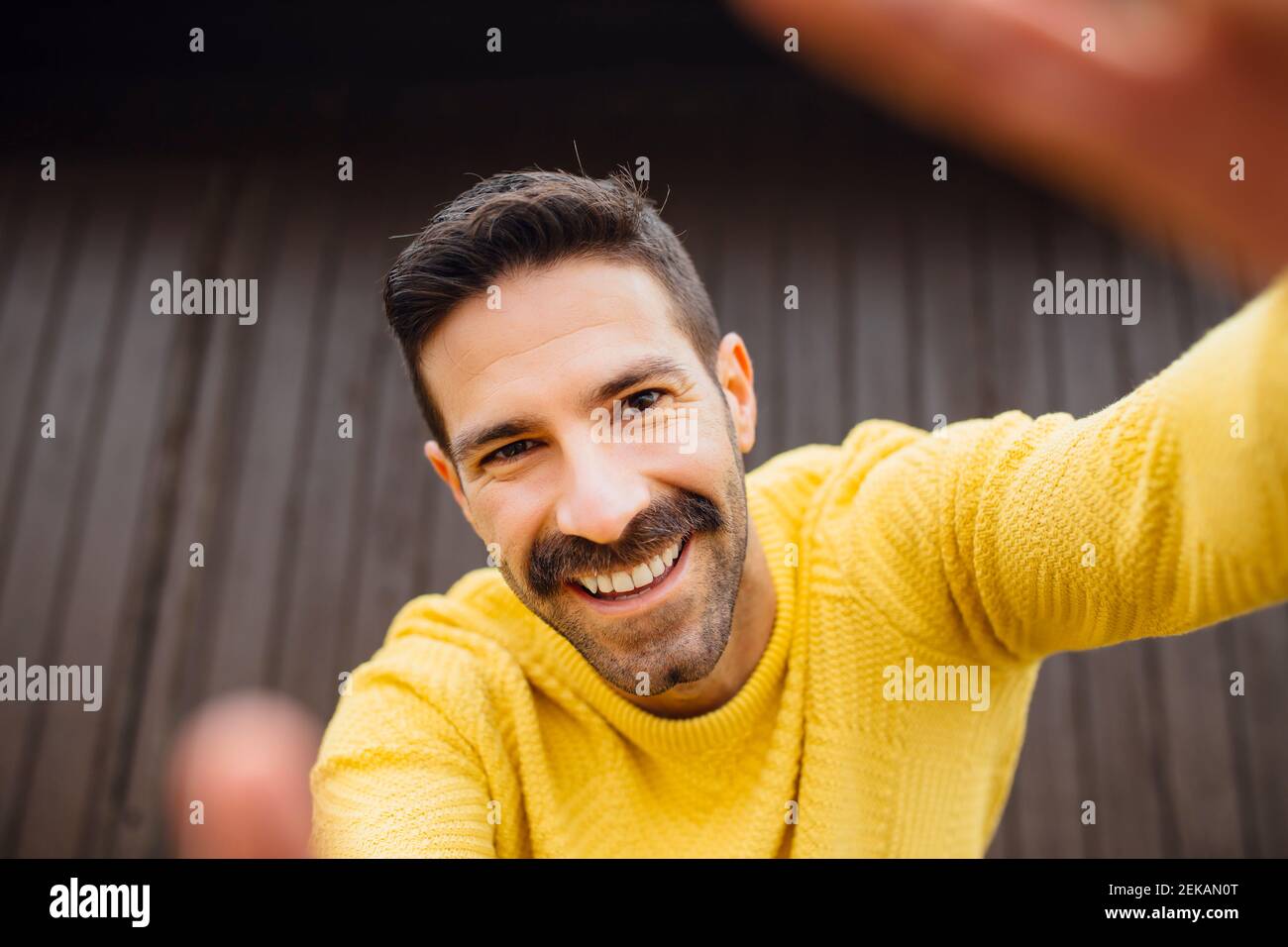 Uomo sorridente con baffi in felpa gialla che prende selfie Foto Stock