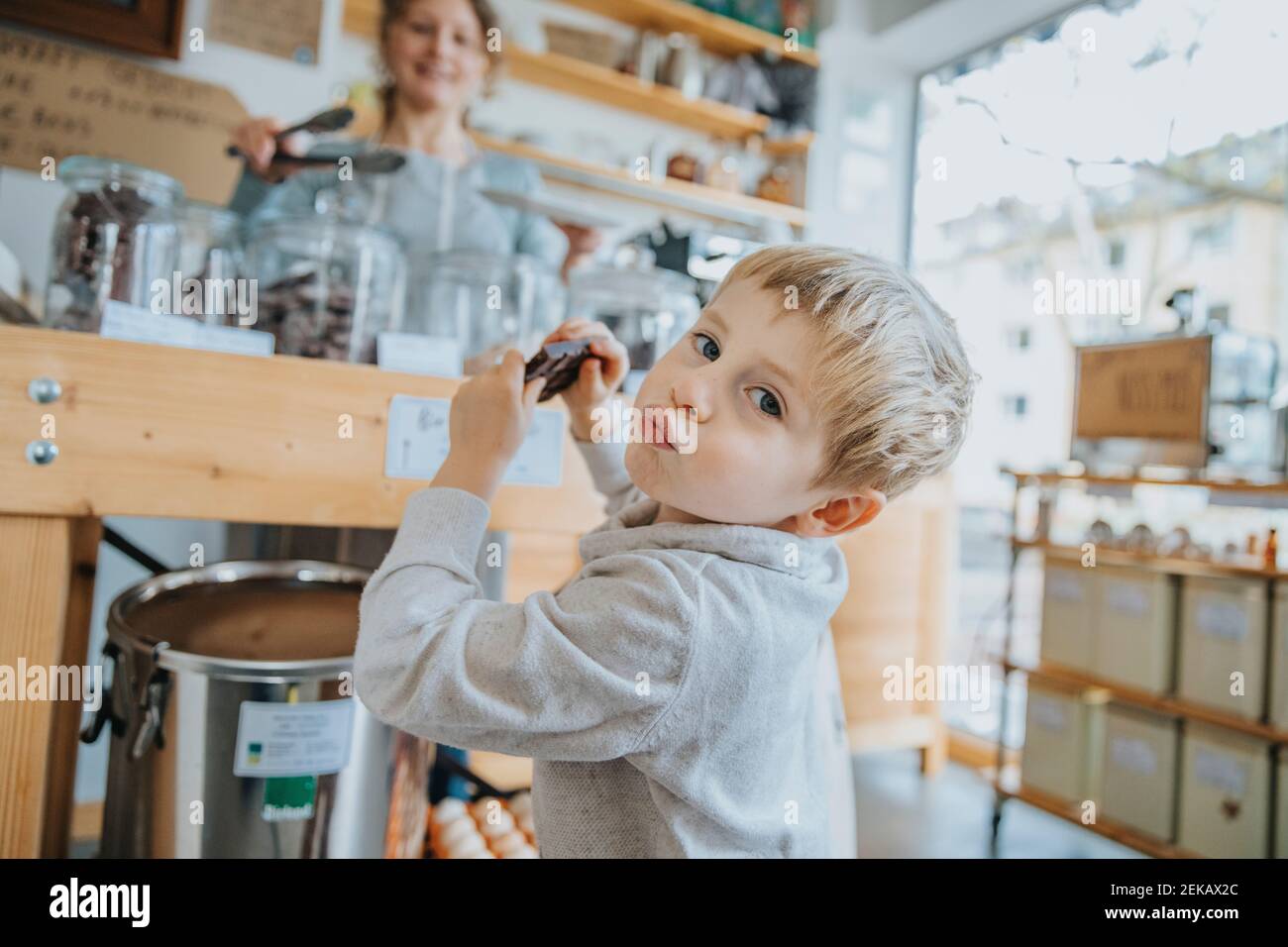 Piccolo ragazzo che ridacchia mentre ha il cioccolato in negozio di caramelle Foto Stock