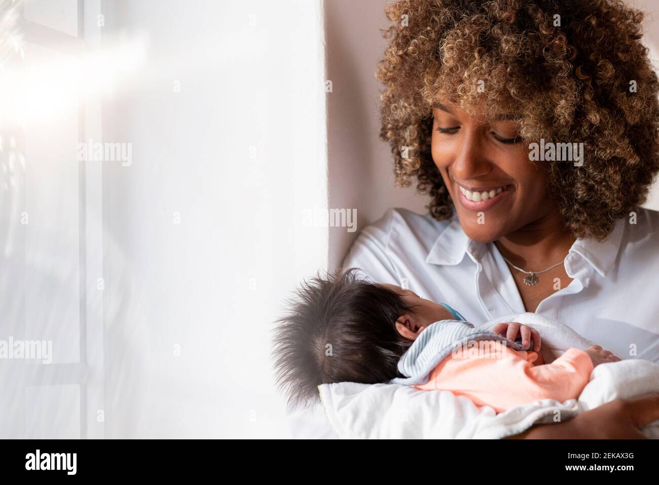 Donna sorridente che tiene il neonato mentre si trova a casa Foto Stock