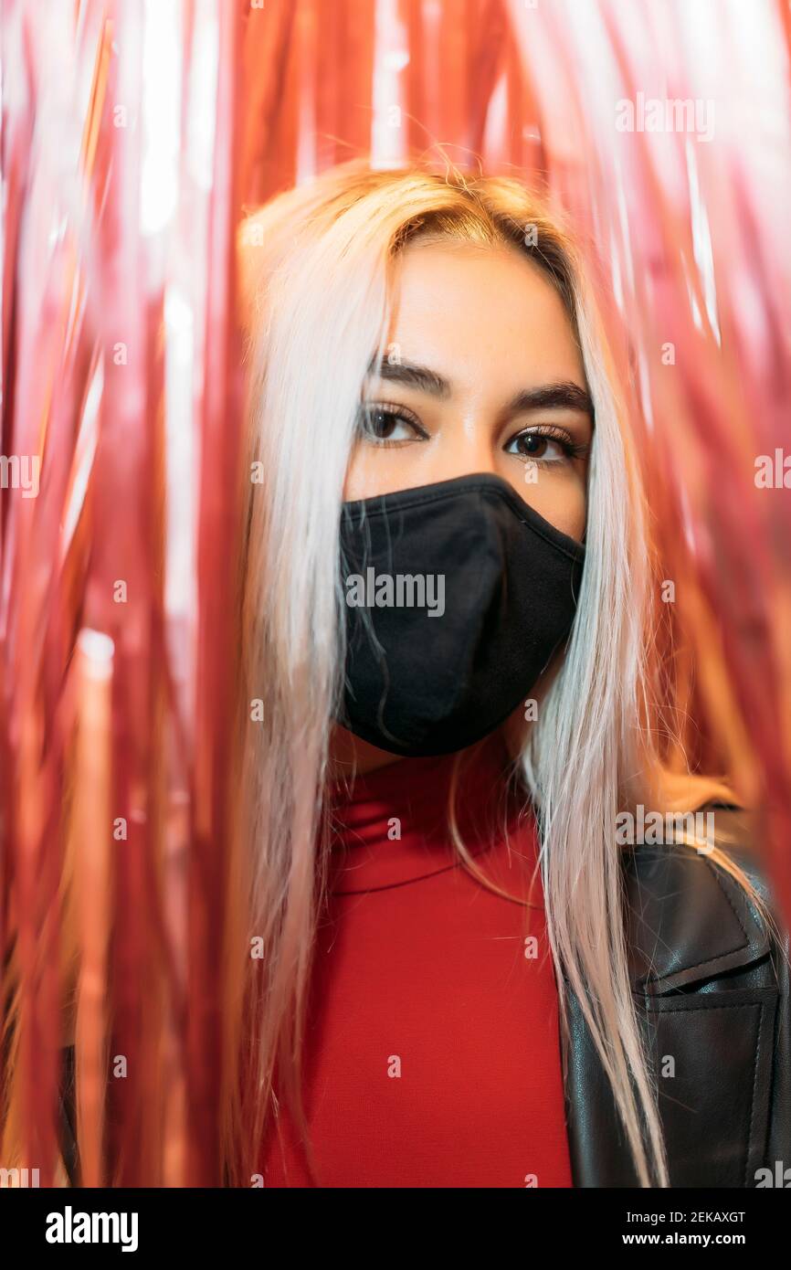 Primo piano ritratto di giovane donna che indossa una maschera nera tra le tende Foto Stock