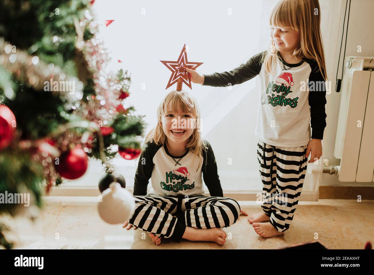 Le sorelle giocano con la decorazione di Natale contro il muro a casa Foto Stock