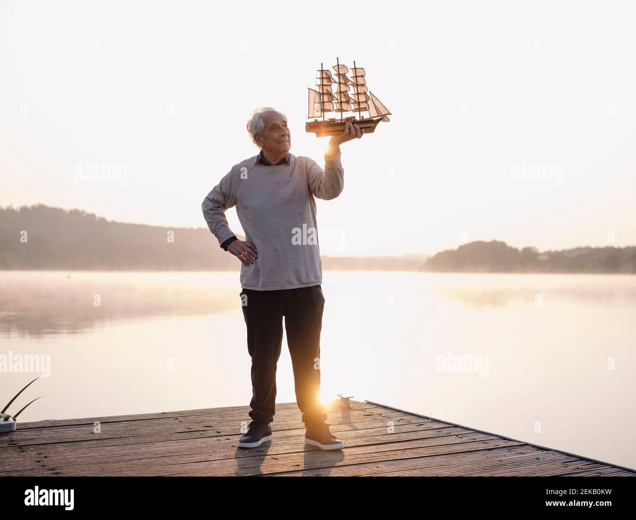Uomo che tiene la nave a vela mentre si è in piedi con la mano sull'anca contro il lago Foto Stock