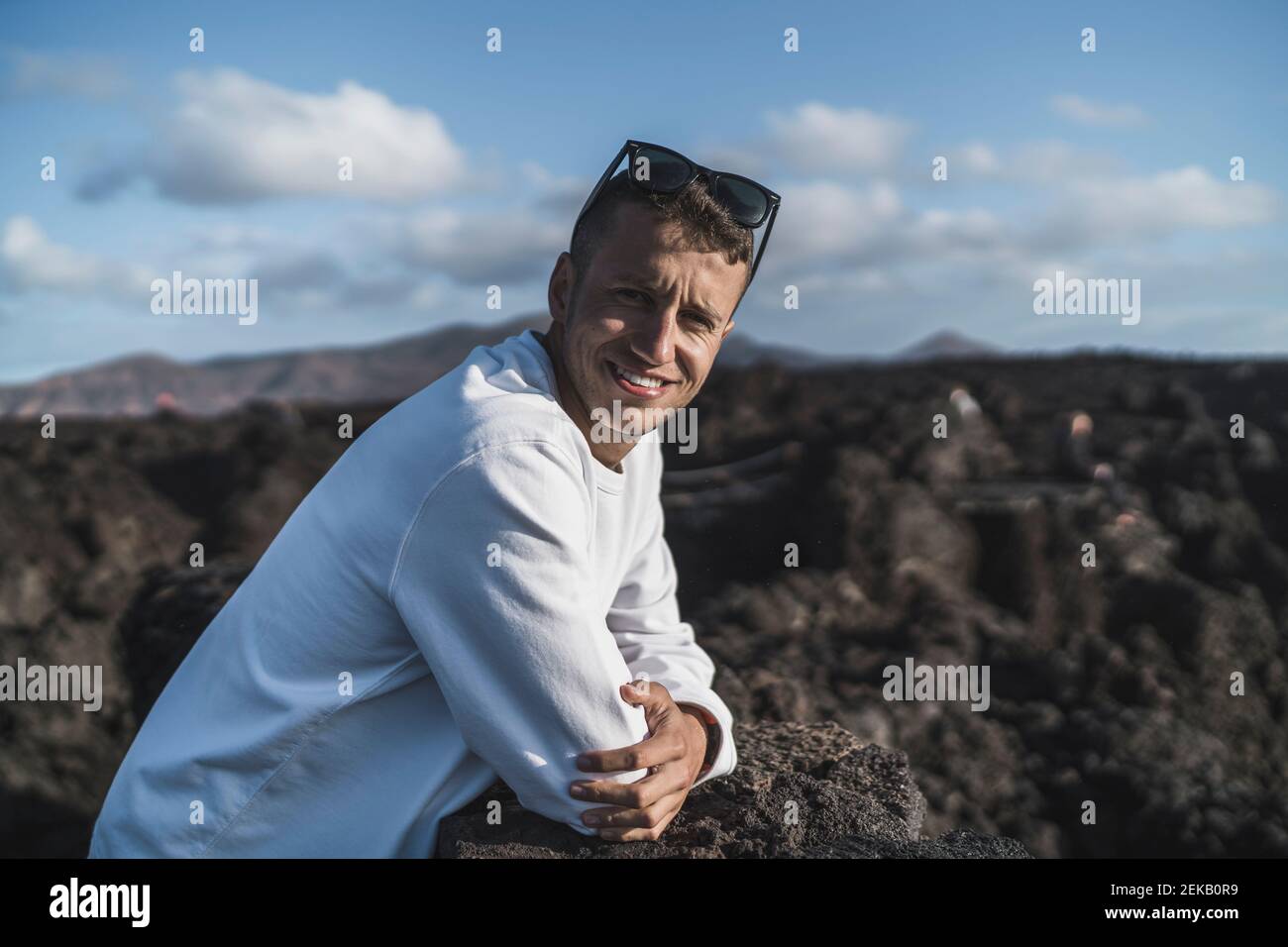 Sorridente turista maschio che si appoggia sulla roccia vulcanica durante la giornata di sole a Los Hervideros, Lanzarote, Spagna Foto Stock