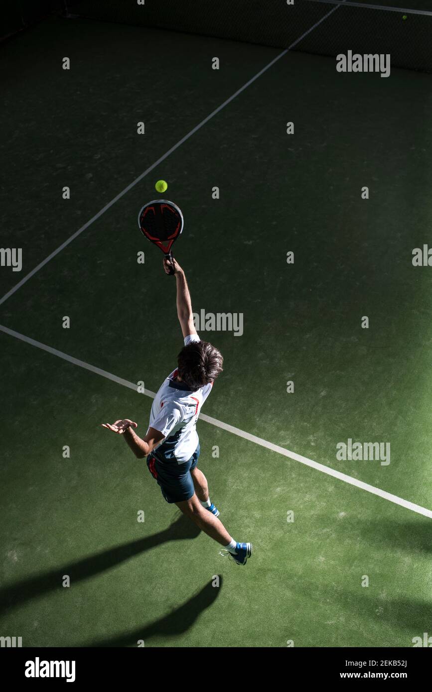 Atleta maschile che serve la palla mentre gioca a padel tennis in campo sportivo di notte Foto Stock
