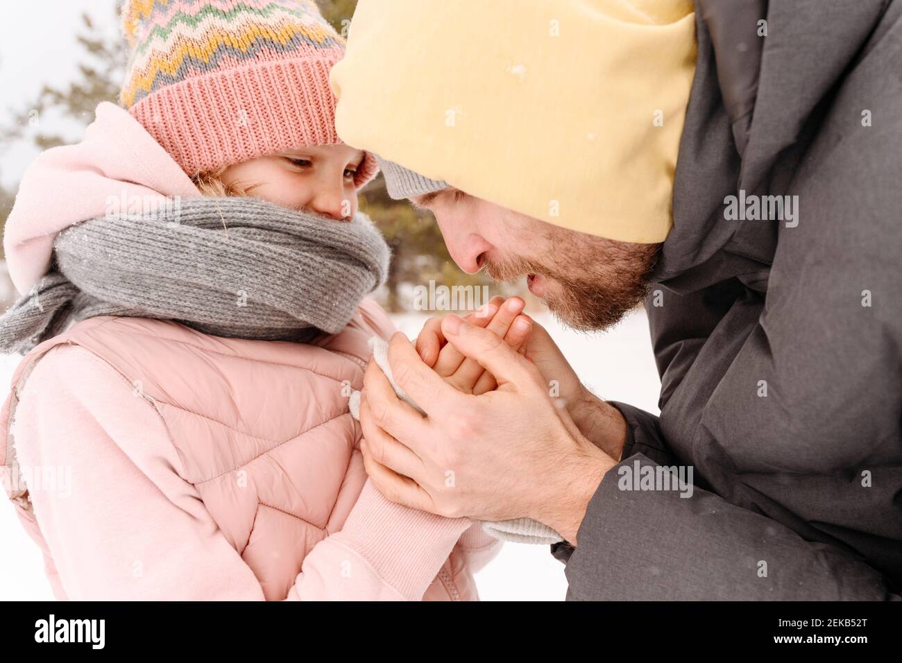 Primo piano di padre che riscalda le mani fredde della figlia durante l'inverno Foto Stock