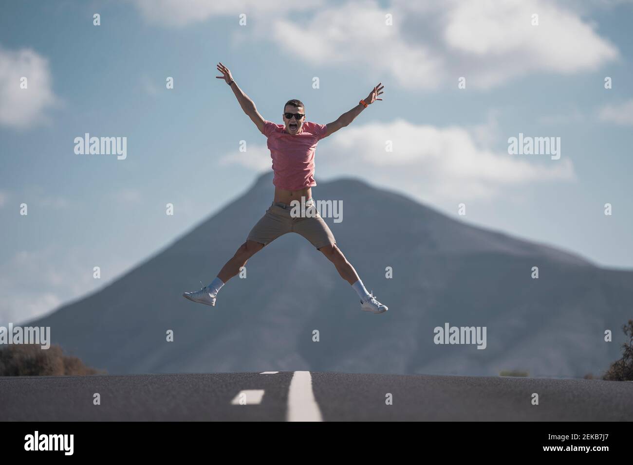 Allegro giovane turista maschile che salta sulla strada contro la roccia vulcanica a Lanzarote durante la giornata di sole, in Spagna Foto Stock