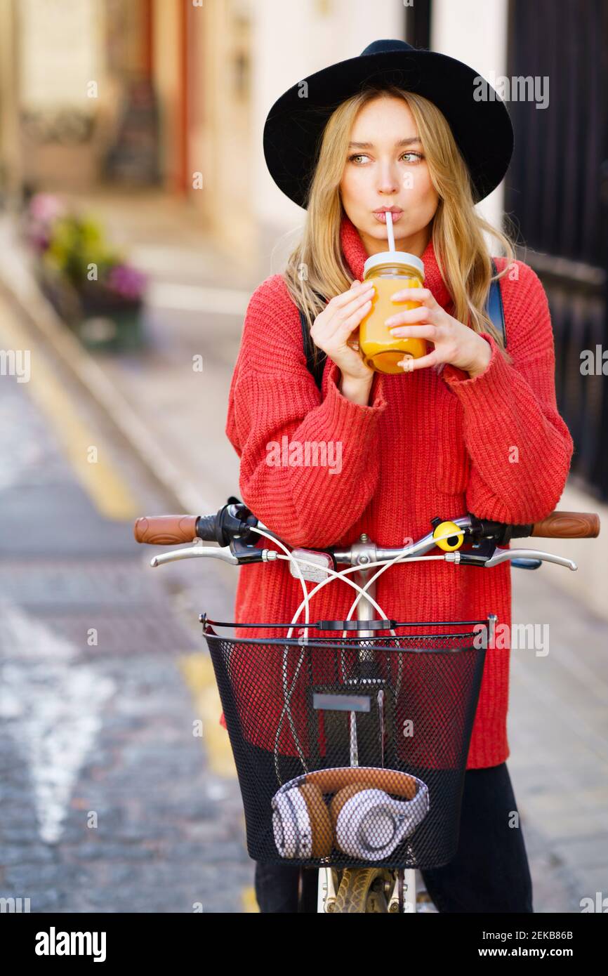 Donna bionda che beve succo mentre è in piedi con la bicicletta sul sentiero Foto Stock