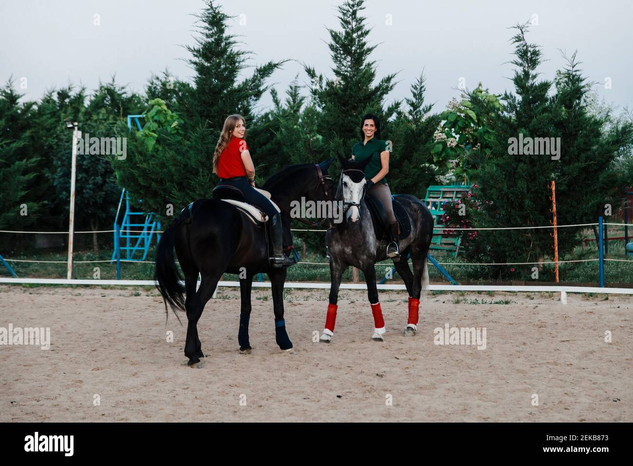 Sorridendo amici femminili seduti sui cavalli di ritorno in fattoria durante fine settimana Foto Stock