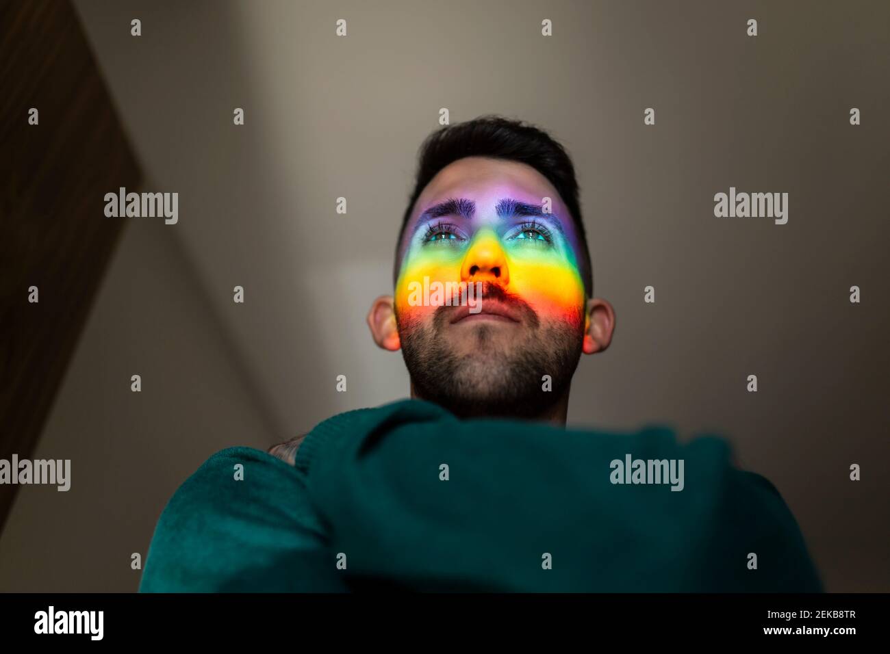 Luce arcobaleno che colpisce il volto di un giovane uomo in piedi all'interno Foto Stock