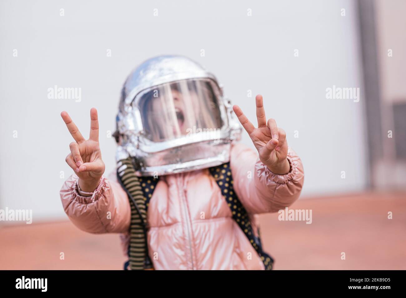 Ragazza con casco spaziale gesturing segno di pace contro parete bianca Foto Stock