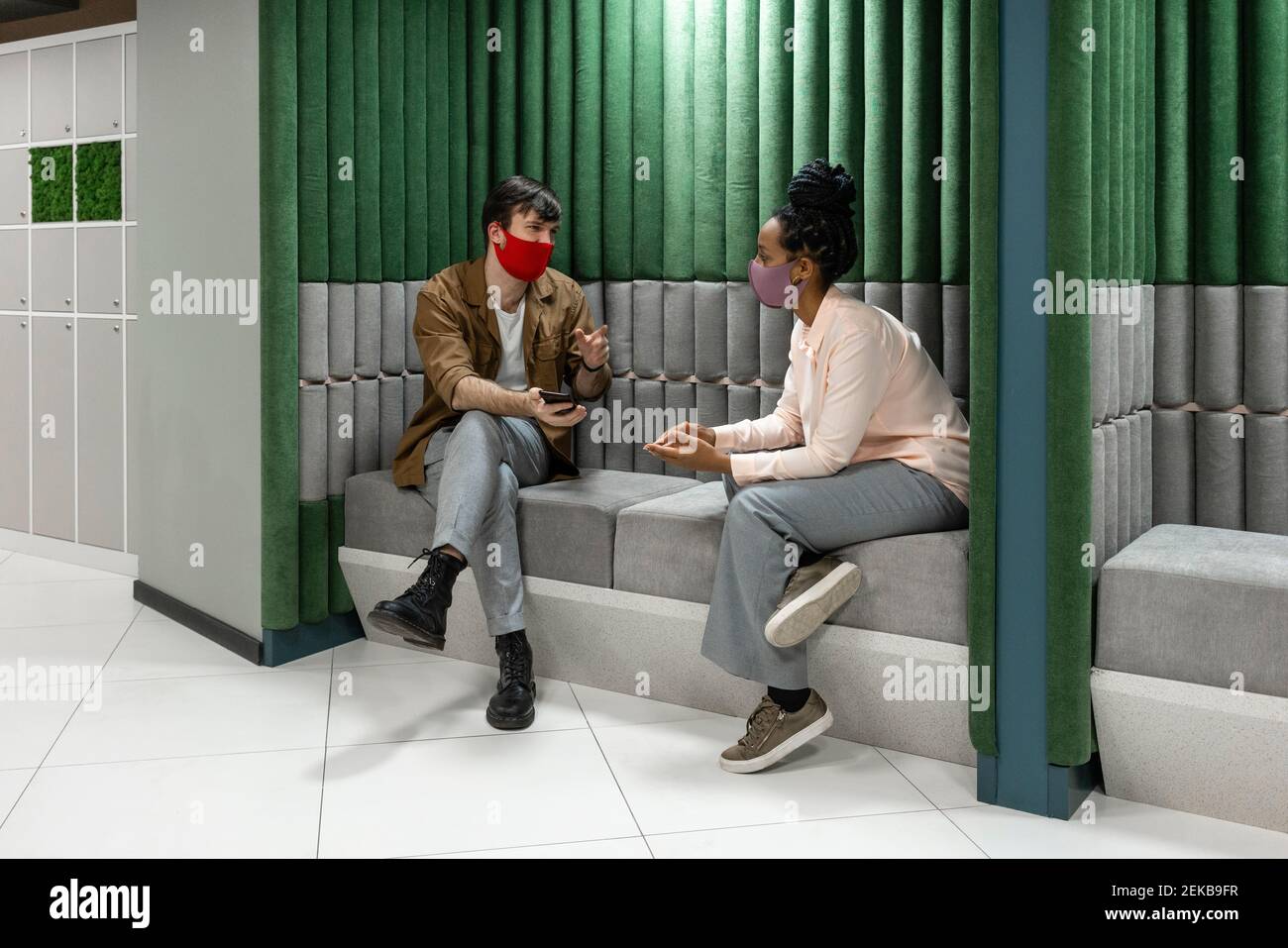 Uomini d'affari nella pianificazione della maschera protettiva mentre si siede sopra divano sul posto di lavoro Foto Stock