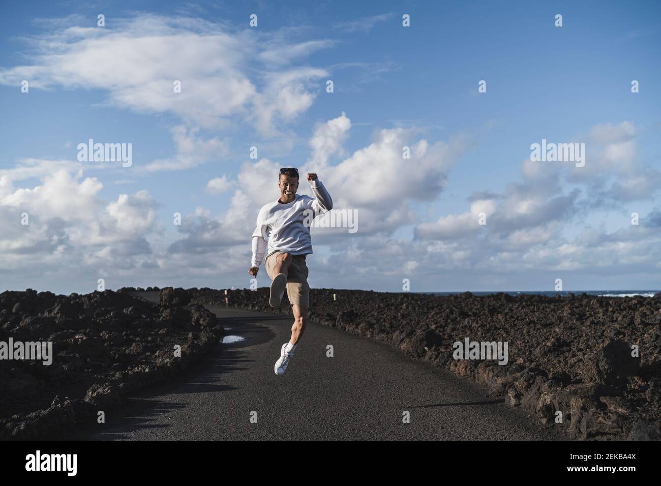 Allegro turista maschio che salta tra roccia vulcanica a Los Hervideros in giorno di sole, Lanzarote, Spagna Foto Stock