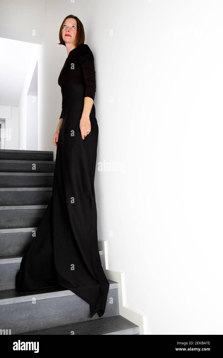 Donna in abito nero appoggiata al muro mentre si sta in piedi scala Foto Stock