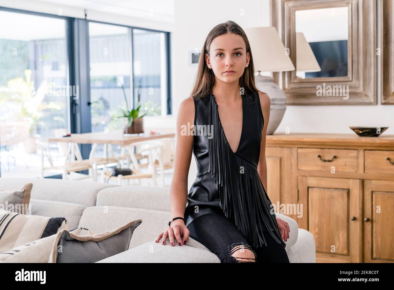 Ragazza adolescente sicura ed elegante che indossa la parte superiore nera seduta sul divano in soggiorno Foto Stock