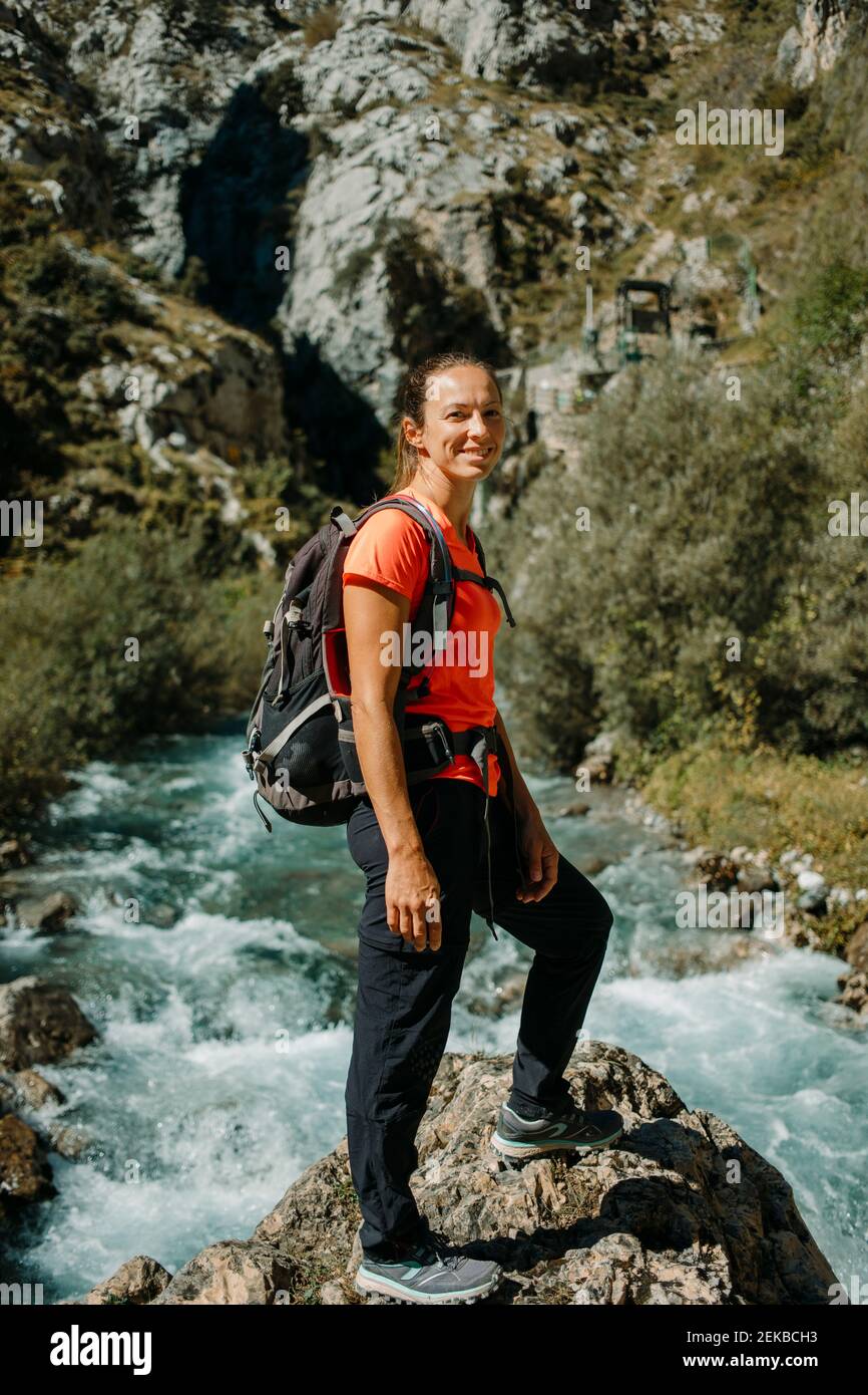 Donna sorridente con zaino in piedi contro il fiume a Cares Trail nel Parco Nazionale Picos De Europe, Asturias, Spagna Foto Stock