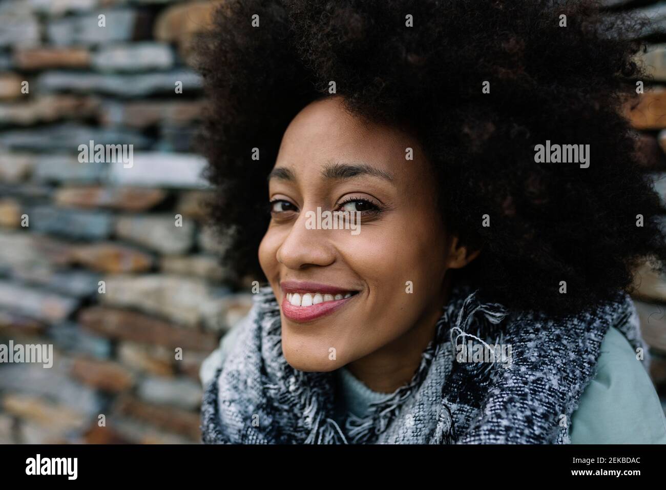 Donna Afro sorridente contro il muro di pietra Foto Stock