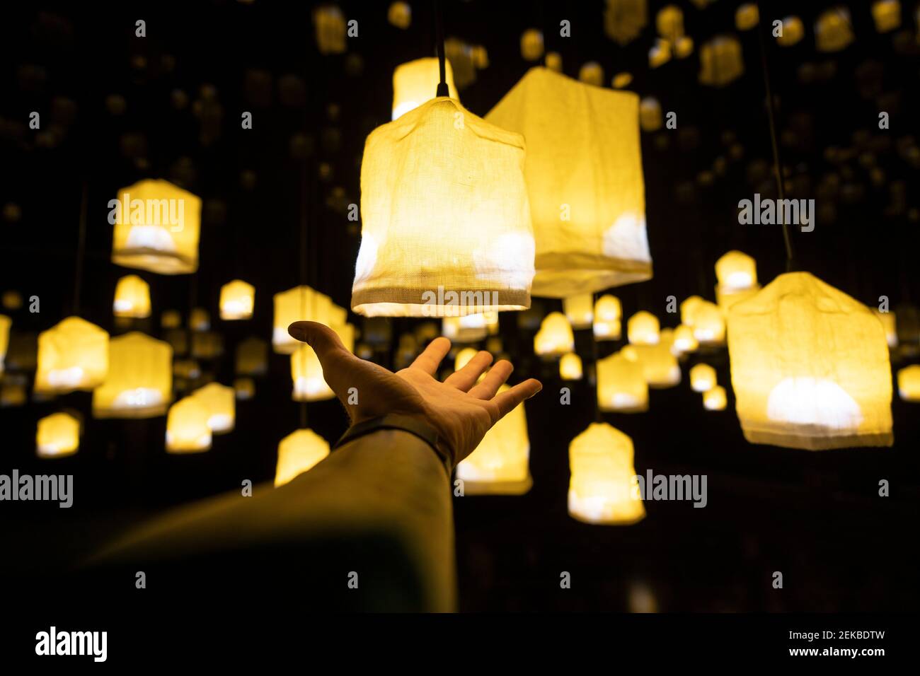 Uomo che presenta lampade di design illuminate appese all'aperto di notte Foto Stock