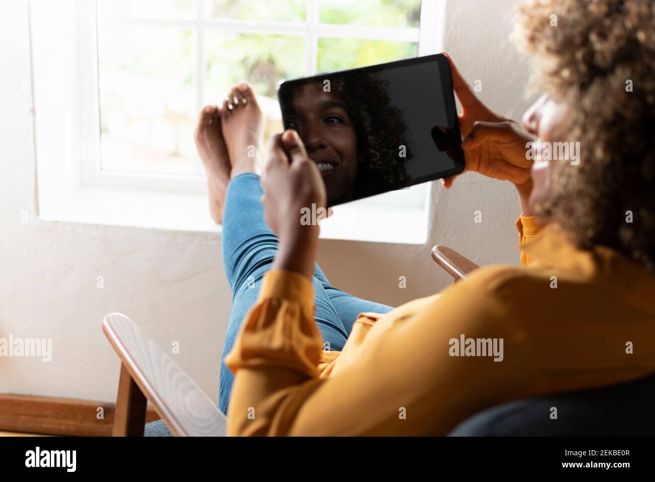 Donna sorridente che usa il tablet digitale mentre si rilassa sulla poltrona casa Foto Stock
