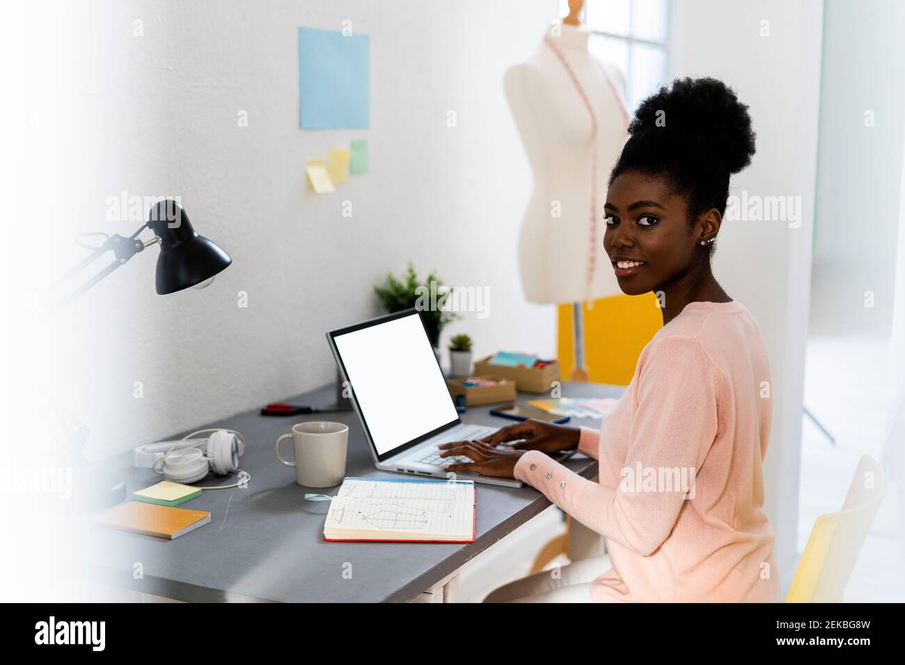 Sorridente designer di moda che usa il computer portatile mentre si è seduti a casa Foto Stock