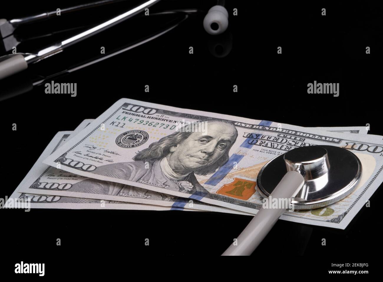 Concetto di sanità, assicurazione ed economia: Le banconote americane da cento dollari con uno stetoscopio sopra di esso sono sdraiate su sfondo nero. Foto Stock