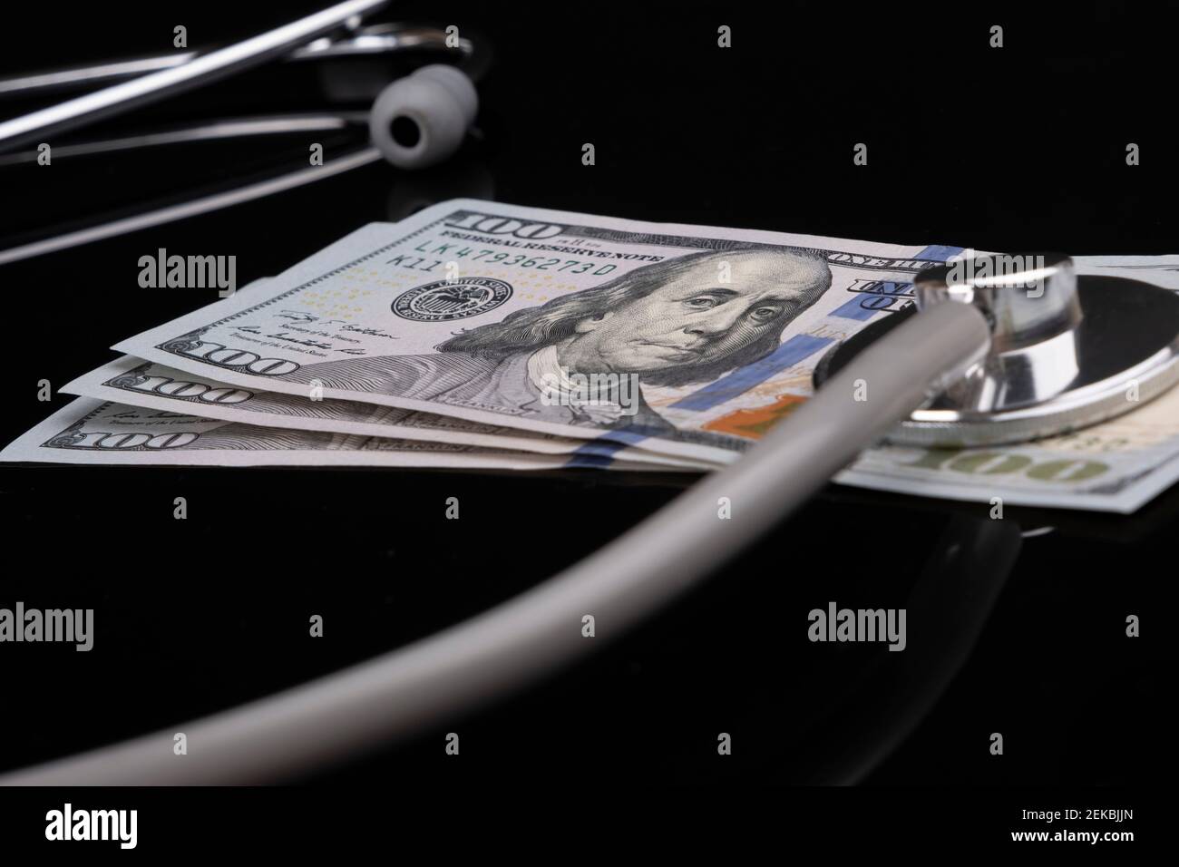 Concetto di sanità, assicurazione ed economia: Le banconote americane da cento dollari con uno stetoscopio sopra di esso sono sdraiate su sfondo nero. Foto Stock