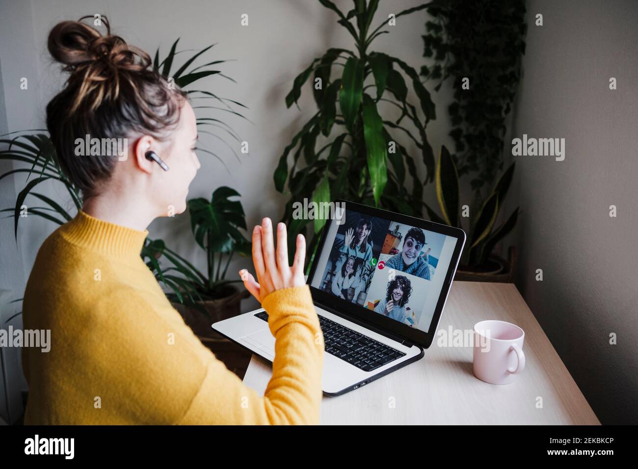 Giovane donna che sventolava la mano agli amici durante la videoconferenza tablet digitale mentre sei seduto a casa Foto Stock