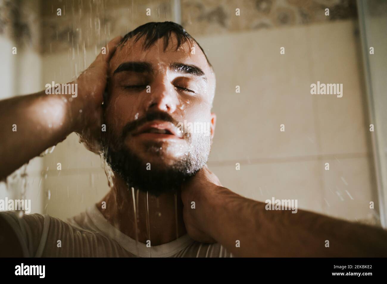 Uomo bearded con gli occhi chiusi prendendo la doccia in bagno Foto Stock
