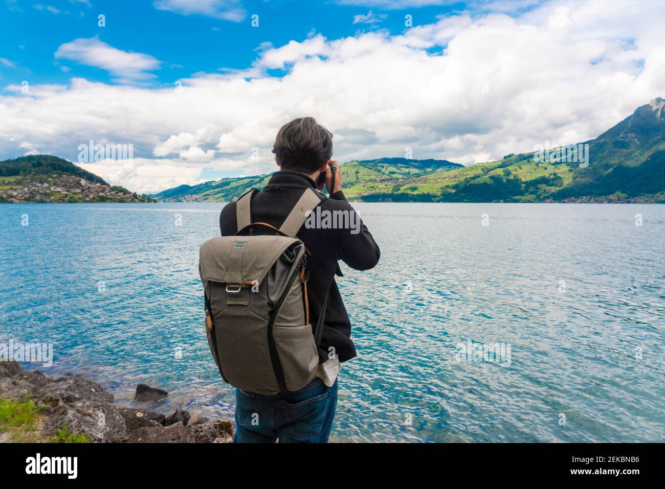 Turista maschile con zaino fotografando il lago Sarner contro cielo nuvoloso In Svizzera Foto Stock