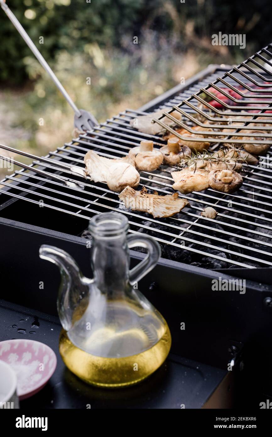 Vasetto di olio d'oliva tenuto oltre barbecue in cortile posteriore Foto Stock