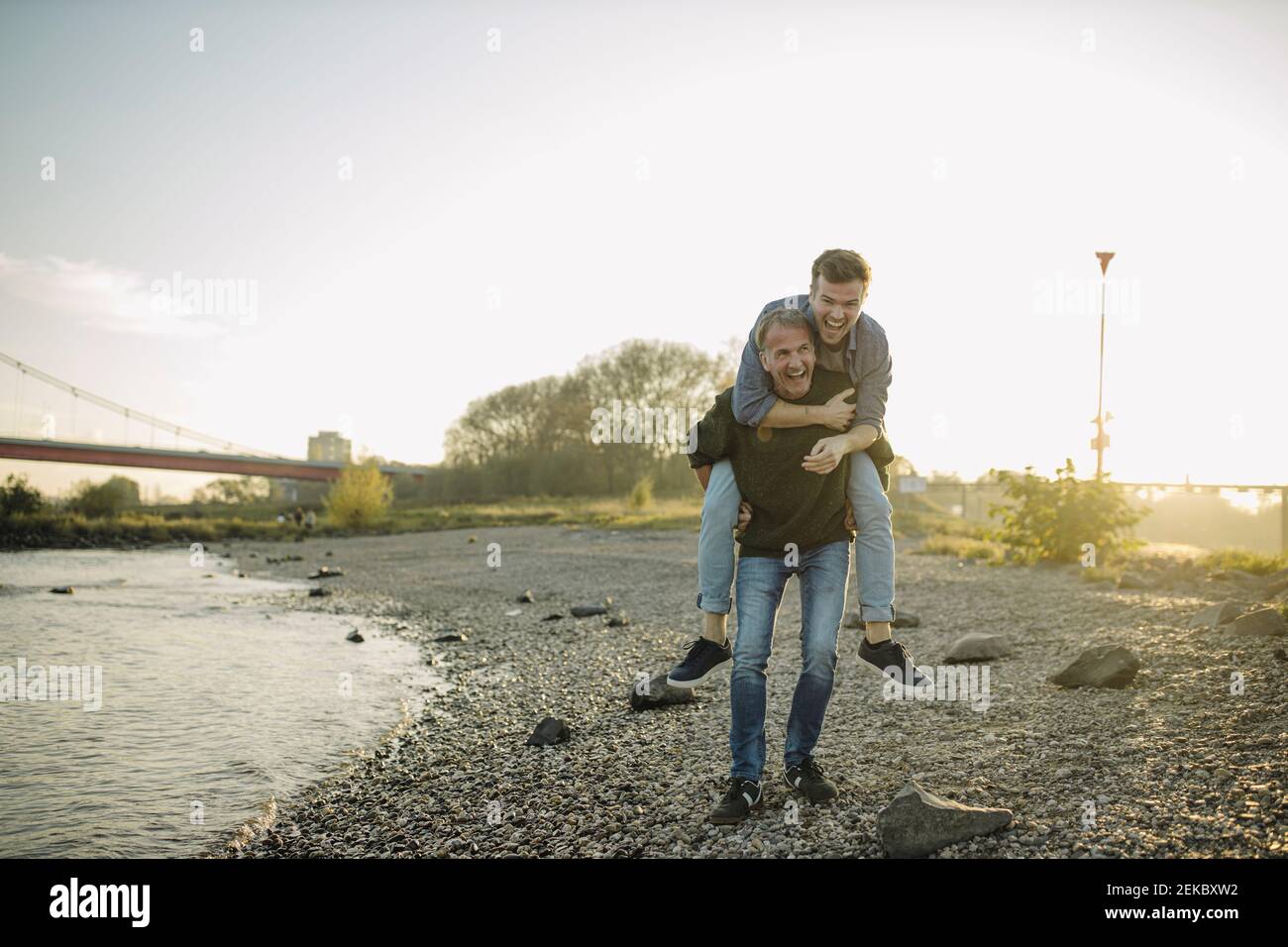 Felice padre che dà giro piggyback a figlio contro il cielo a. sera Foto Stock