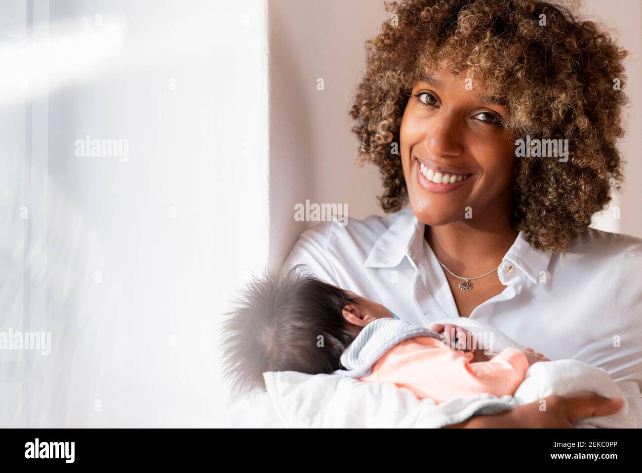Donna felice che tiene il bambino neonato mentre si trova a casa Foto Stock