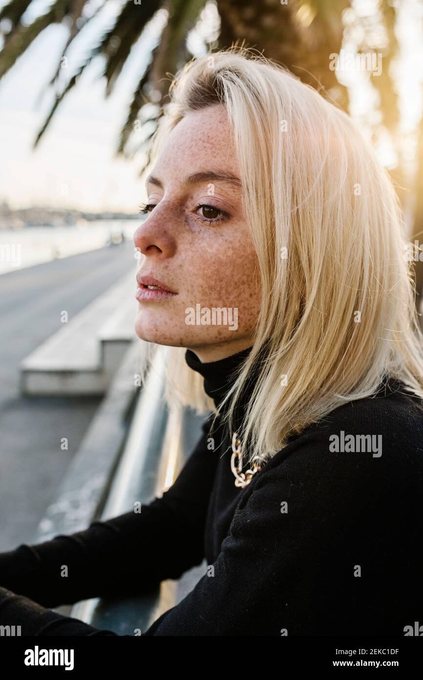 Giovane donna con le bracelle appoggiate alla ringhiera contro l'albero di palma Foto Stock