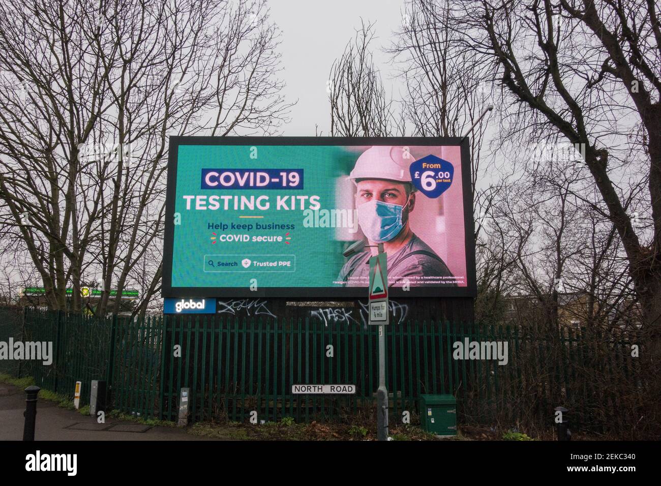 Un annuncio per un kit di test Covid-19 su un globale cartellone elettronico digitale con un giovane uomo che indossa un bianco hardhat Foto Stock