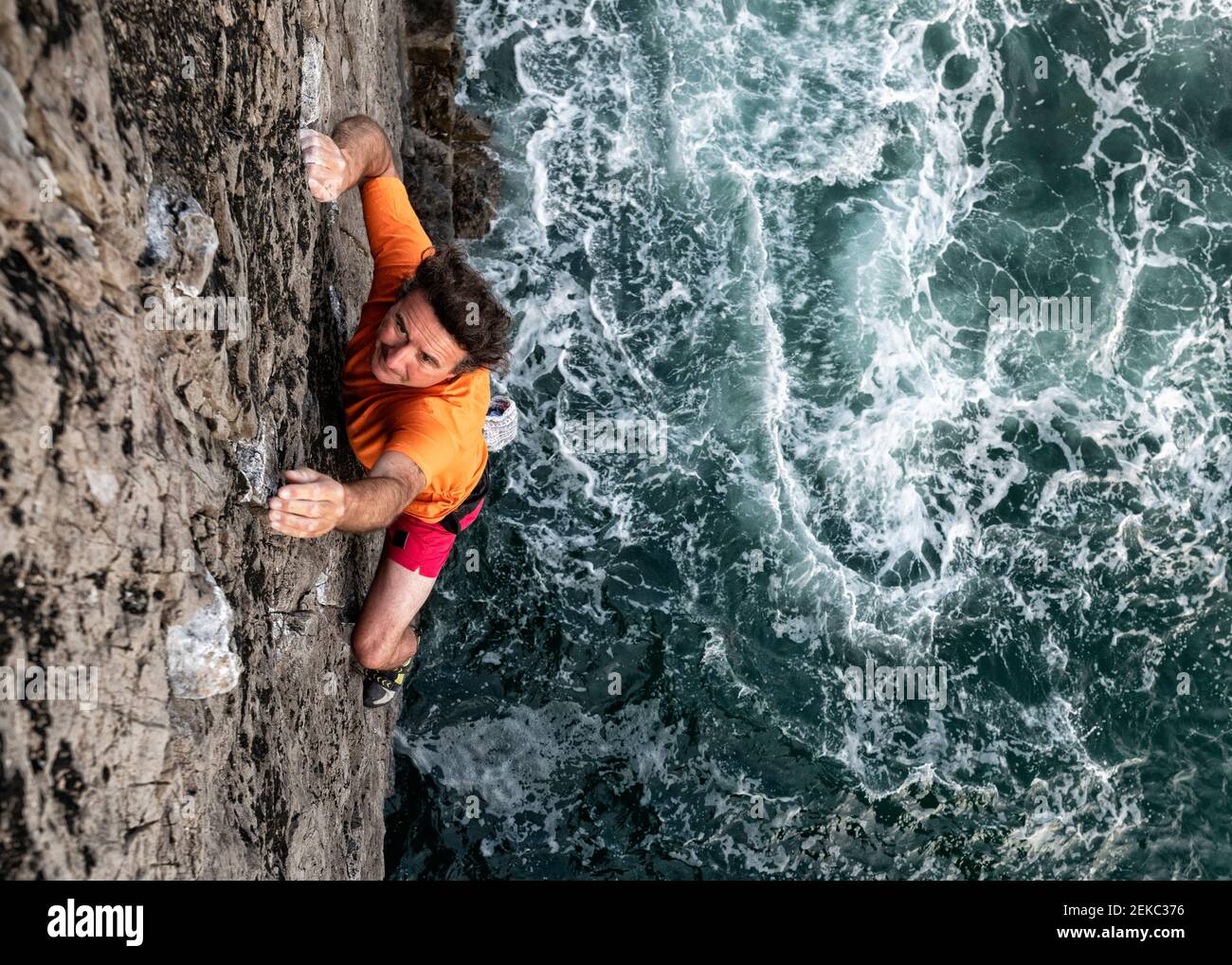 Appassionato scalatore di roccia maschile arrampicata scogliera rocciosa dal mare Foto Stock