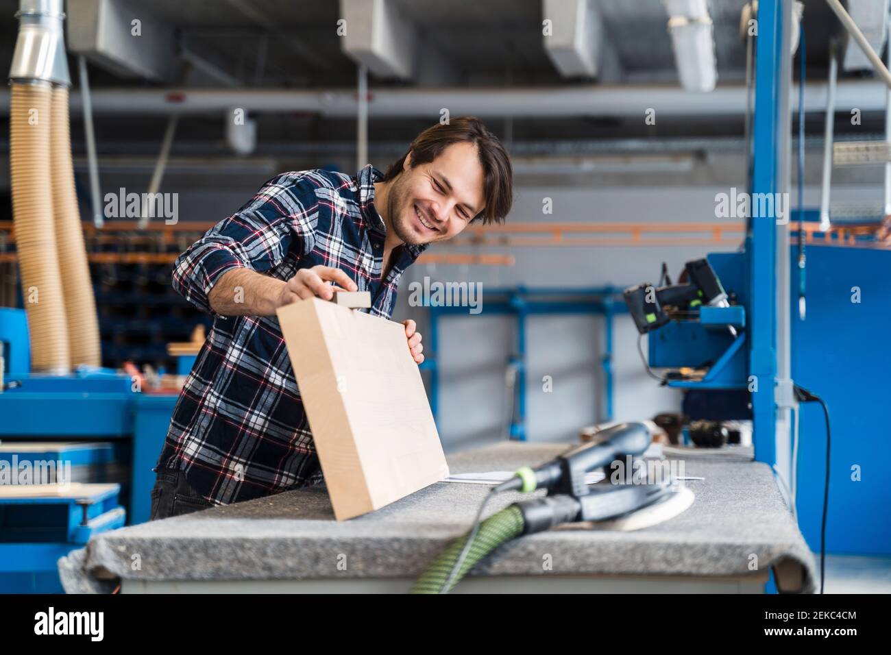 Sorridente lavoratore manuale che misura il legno mentre si trova in piedi all'industria Foto Stock