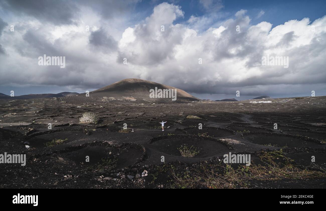 Turista maschile con le braccia distese in piedi sulla cenere nera del vulcano El Cuervo, Lanzarote, Spagna Foto Stock