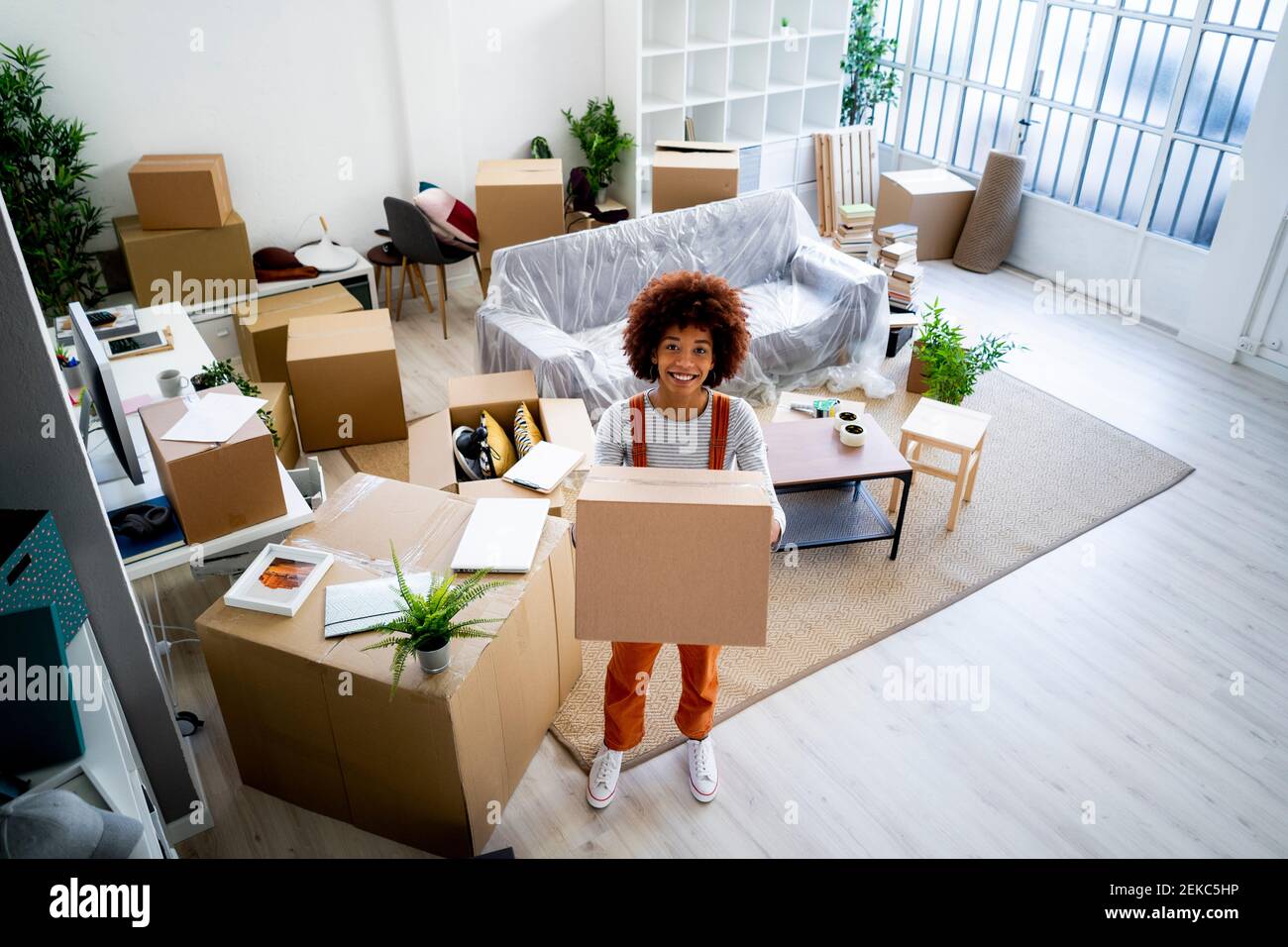 Felice giovane donna afro che trasporta il cartone mentre si muove in nuovo casa Foto Stock